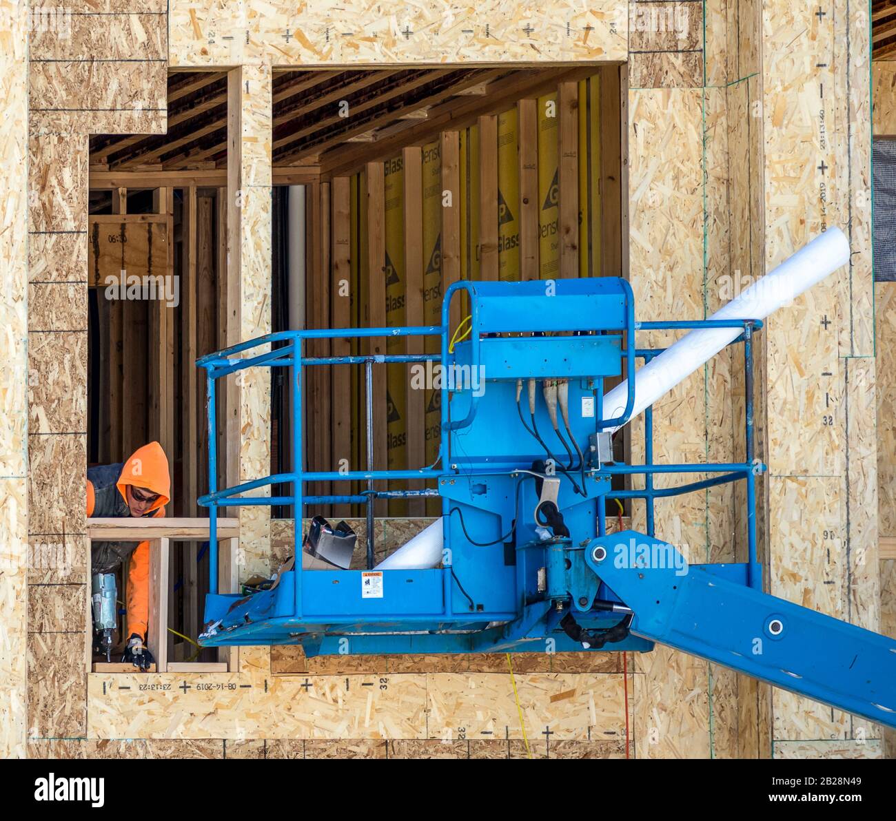 Fraser, Colorado - 22 février 2020 : un homme travaillant dans des lunettes protégées et des chiffons orange travaillant à l'extérieur sur un chantier de construction derrière le berceau bleu Banque D'Images