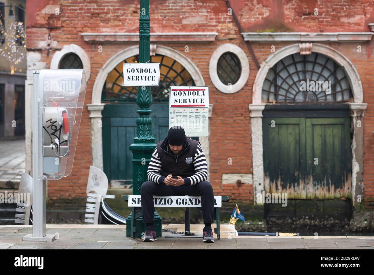 Gondolier est assis sur le côté du canal à Venise et regarde son téléphone. Prise en janvier 2020. Banque D'Images