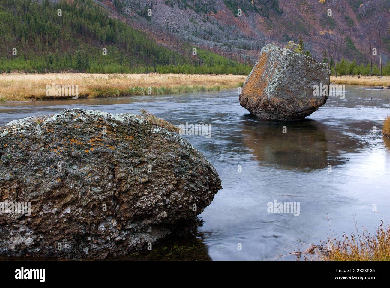 Le gros rocher naturellement coloré repose de manière immovante dans la rivière peu profonde Banque D'Images