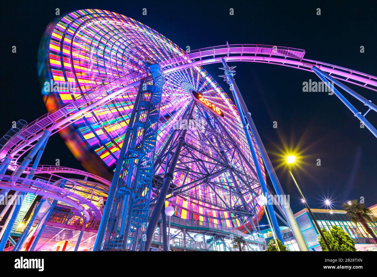Vue de dessous du géant coloré Ferris Wheel and Roller Coaster illuminé la nuit dans le district de Minato Mirai. Banque D'Images