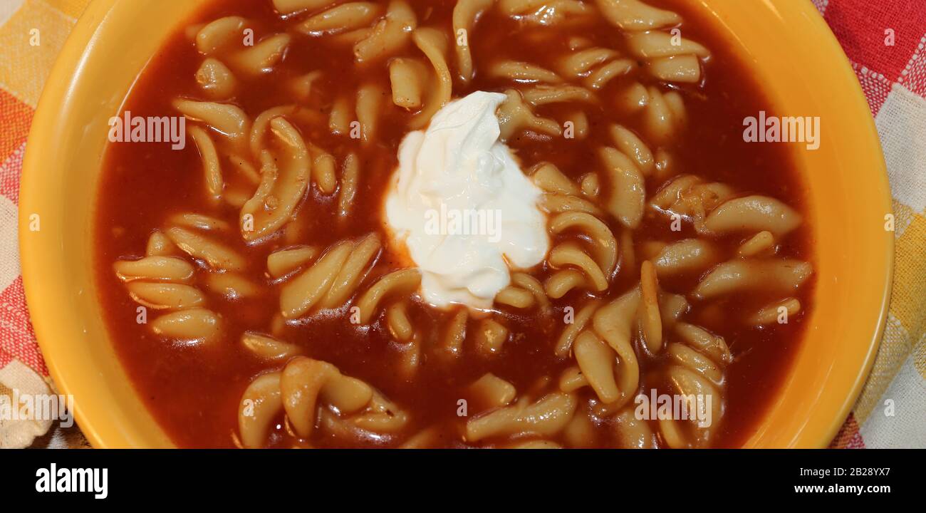 Soupe de tomate traditionnelle avec crème saure au milieu, avec nouilles de farine de seigle, dans plaque jaune / bol vue de dessus de près. Banque D'Images