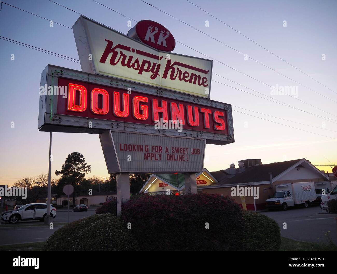 Savannah, GA - 22 FÉVRIER 2020: Un panneau au néon éclairé pour Krispy Kreme Donuts brille sur un coin de rue au crépuscule à Savannah, Géorgie, avec le donut Banque D'Images