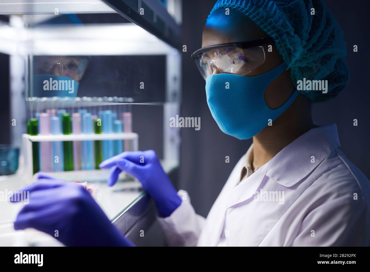 Vue latérale portrait d'un scientifique féminin portant un masque facial et un équipement de protection travaillant sur la recherche en laboratoire, espace de copie Banque D'Images