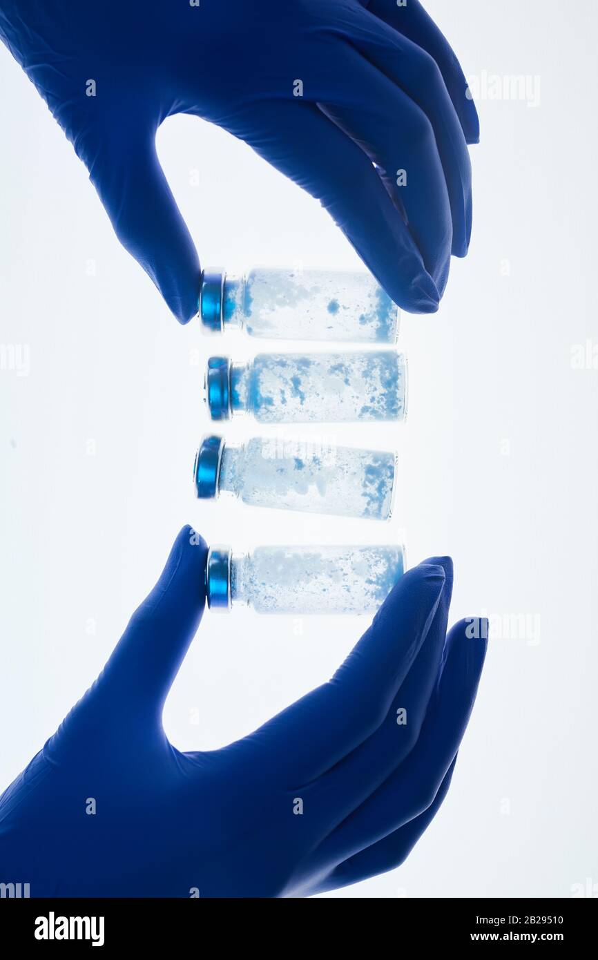 Vue de dessus arrière-plan des mains gantées tenant des flacons en verre en rangée sur la table blanche dans le laboratoire médical, espace de copie Banque D'Images