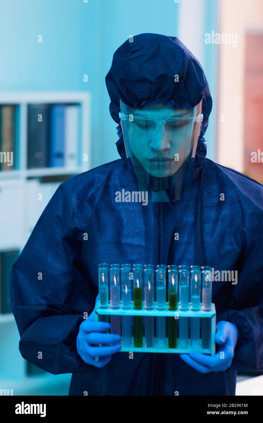 Portrait vertical du scientifique en costume de protection complet tenant des tubes à essai tout en travaillant sur la recherche en laboratoire Banque D'Images