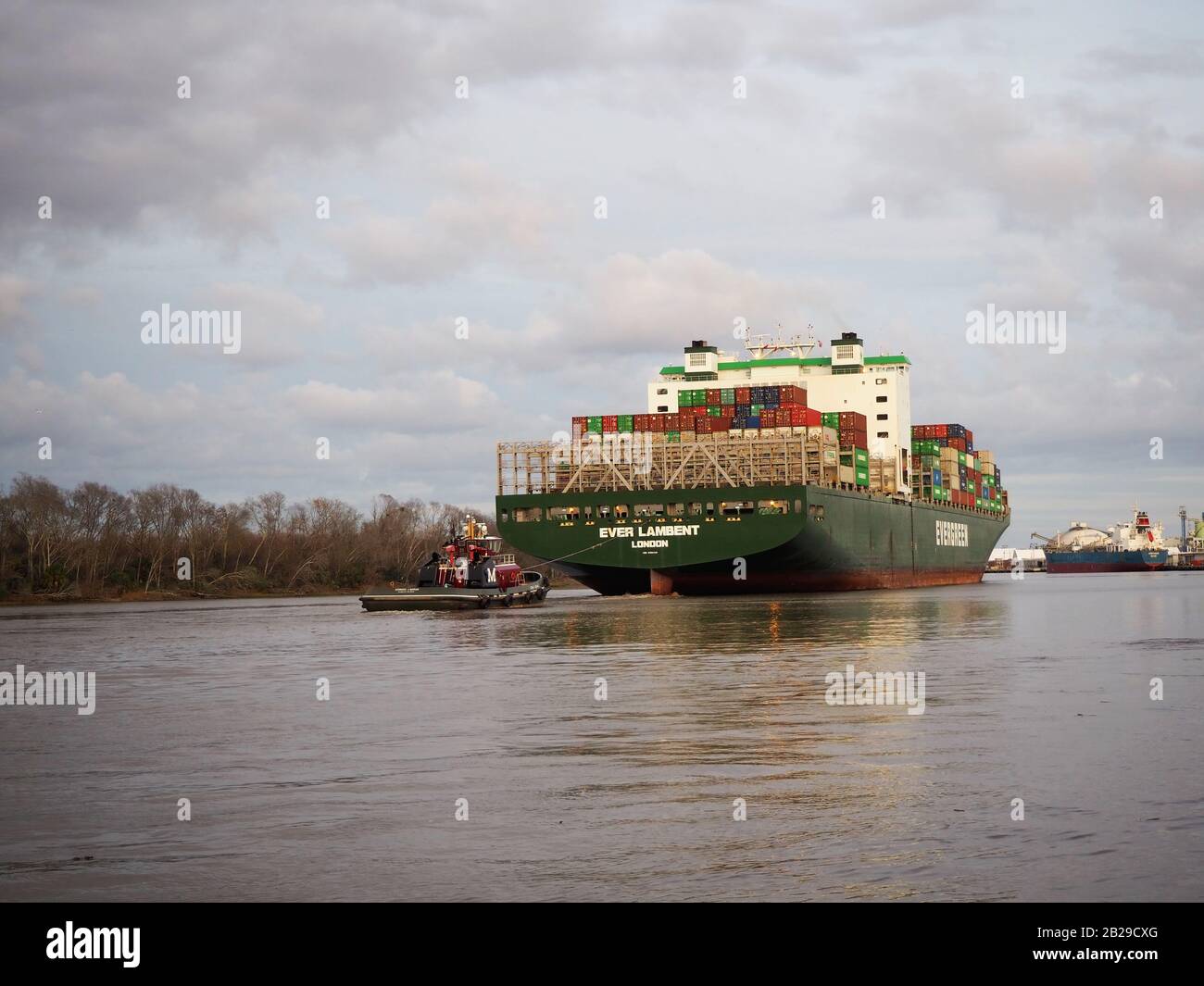 Savannah, GA - 23 FÉVRIER 2020: Un bateau remorqueur aide à guider de derrière un grand cargo chargé de conteneurs d'expédition hors du port de Savannah o Banque D'Images