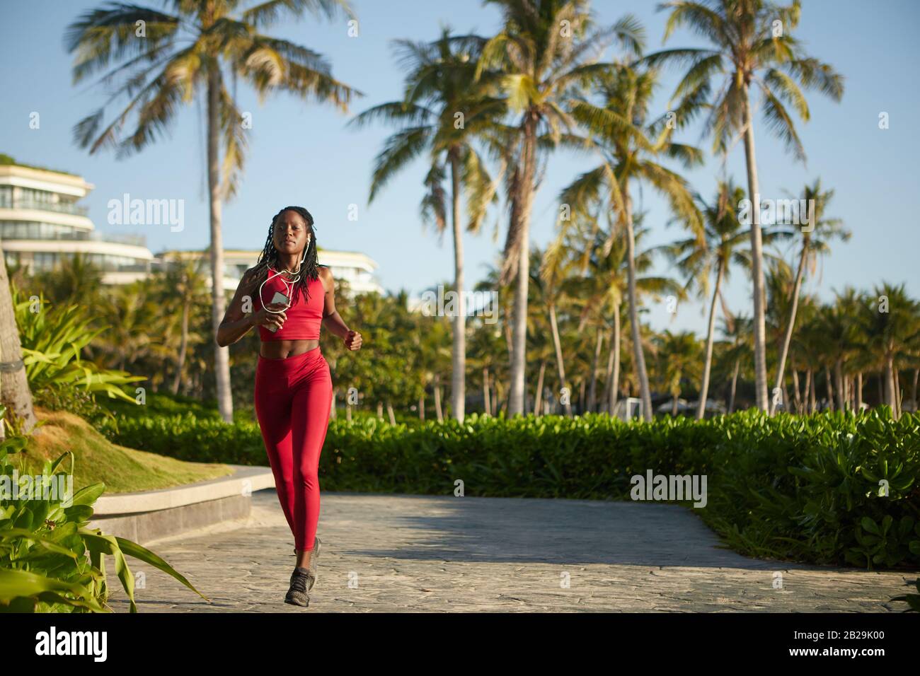 Belle jeune femme dans des vêtements de sport rouge vif jogging dans le parc Banque D'Images