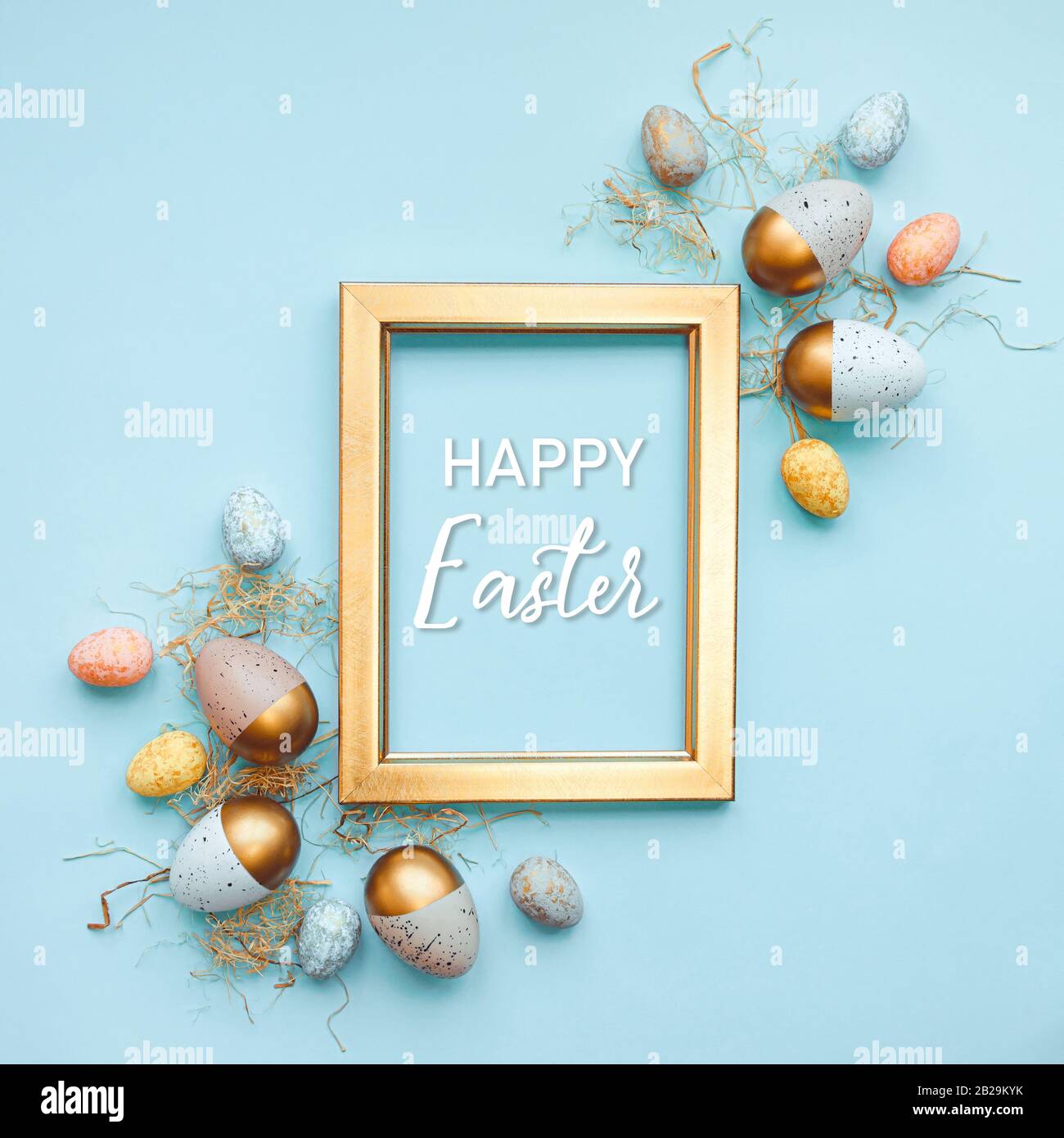 Vue sur le dessus des œufs de Pâques colorés dans différentes couleurs disposés autour d'un cadre photo doré. Fond bleu. Texte de joyeuses Pâques. Banque D'Images