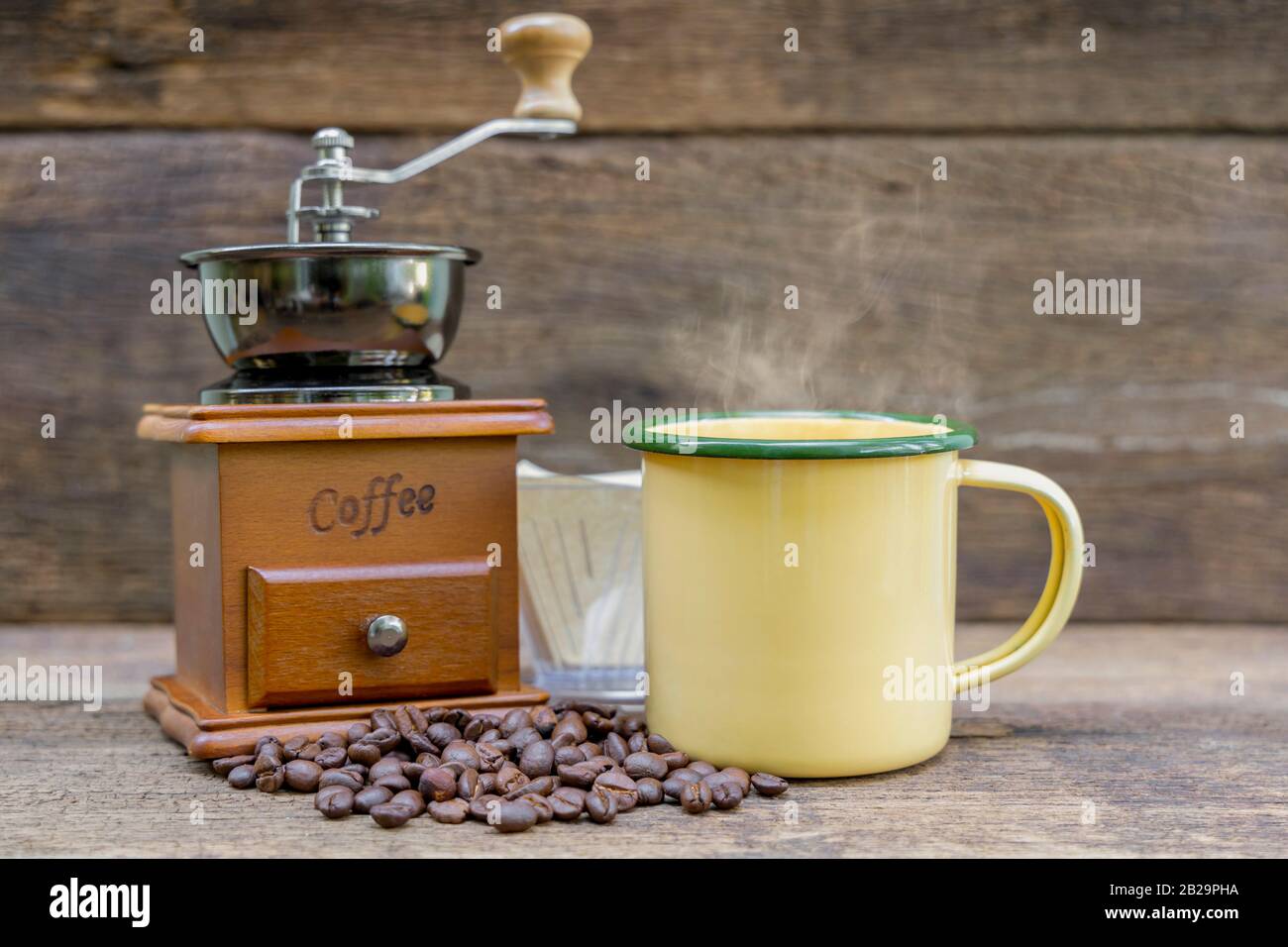 Une tasse de café chaud en étain jaune avec moulin à café et grain de café sur la table en bois. Banque D'Images