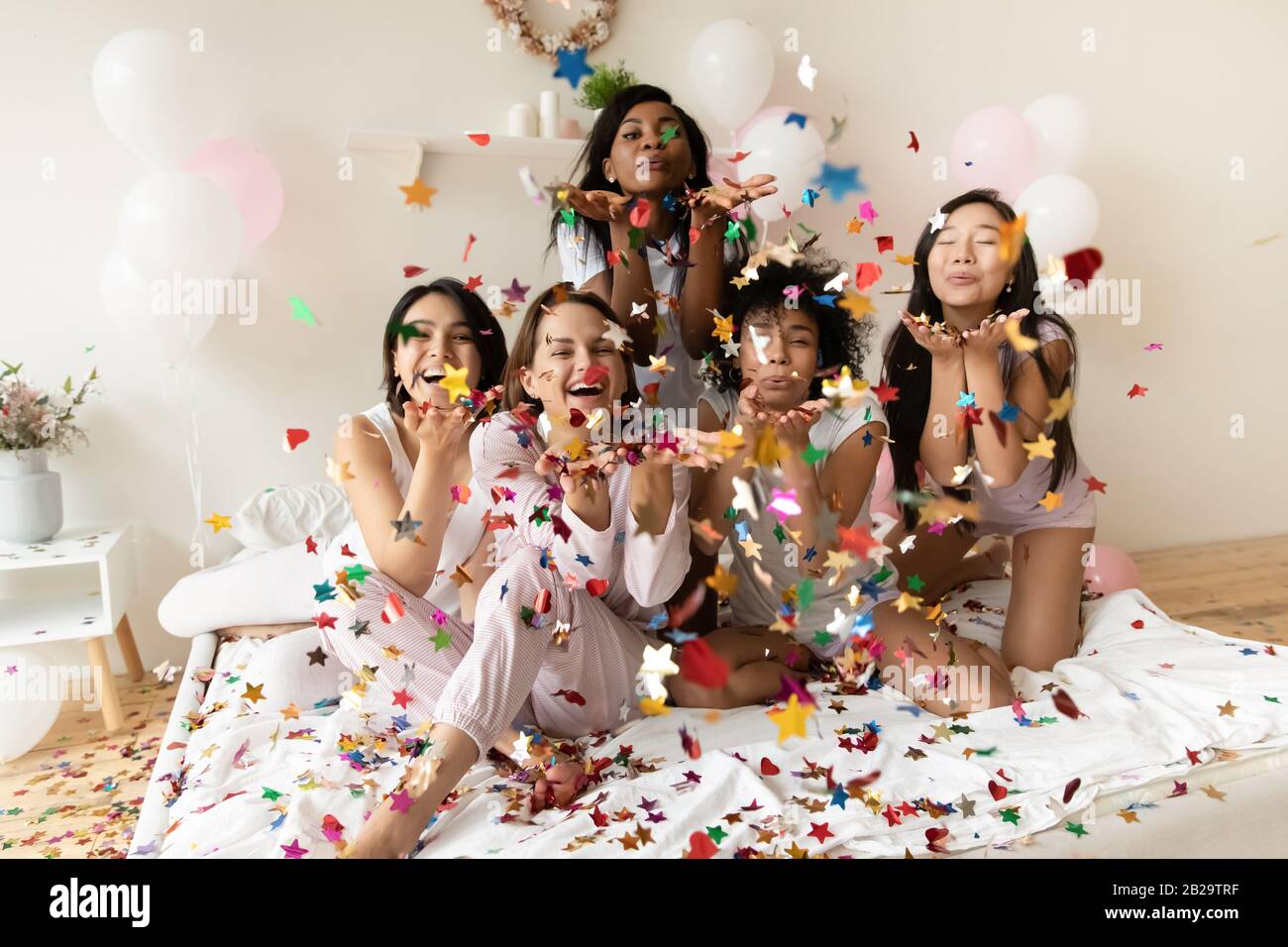 Portrait heureux diverses filles soufflant des confettis à l'appareil photo à la fête Banque D'Images