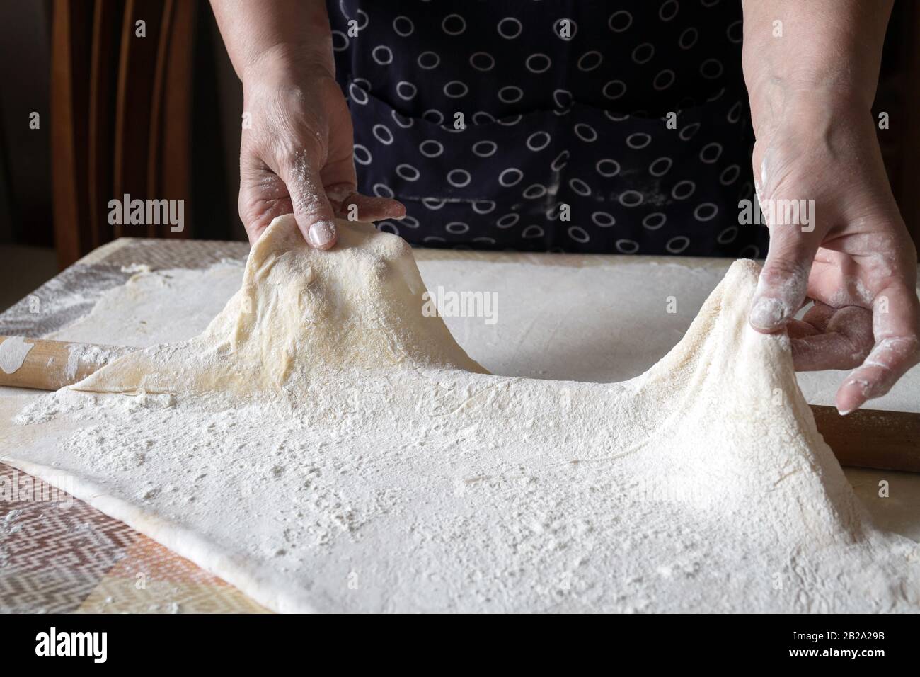 Femme senior étire la pâte pendant le déroulement de la pâte dans sa cuisine maison. Production de nouilles ou de pâtes maison par grand-mère. Gros plan, focu sélectif Banque D'Images