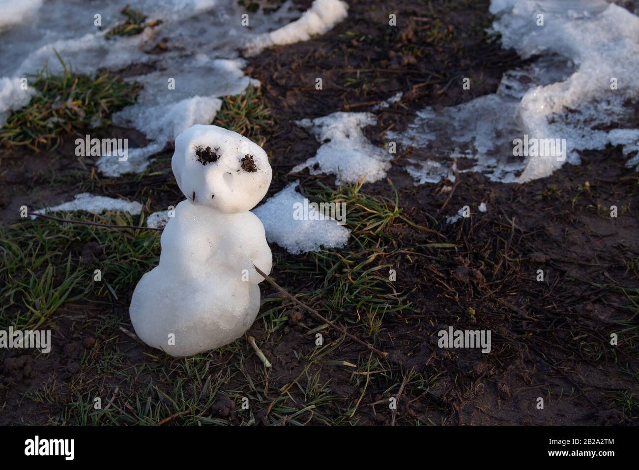 Dernier bonhomme de neige miniature debout dans la boue et l'herbe, fondre au soleil du soir au printemps Banque D'Images