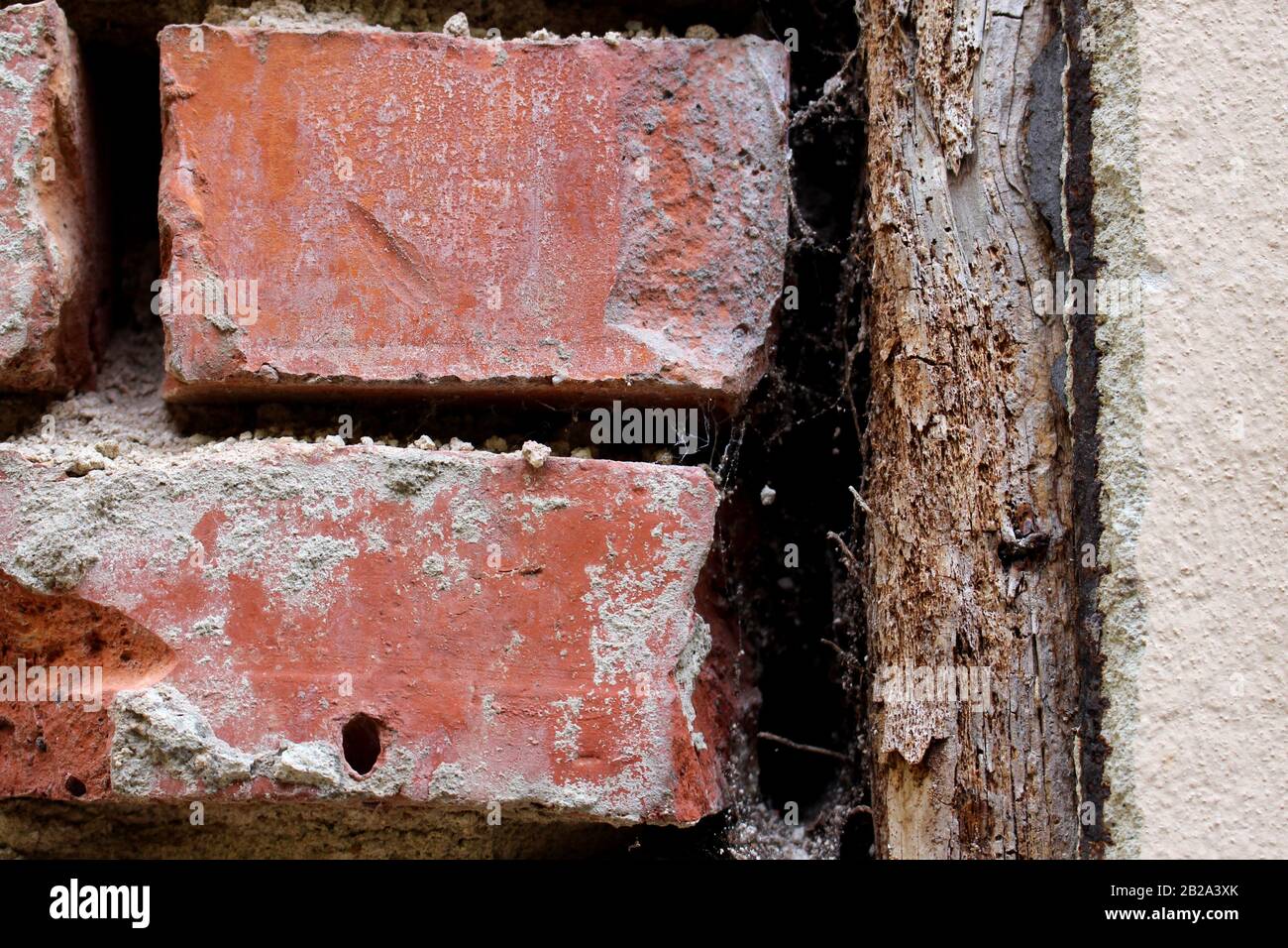 Gros plan de briques cassées dans un mur de briques vieux et abîmé et une planche en bois comme bordure Banque D'Images