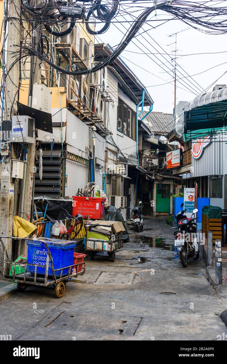 Allée désordonnée et mal rangée avec des poubelles et des câbles électriques suspendus à un poteau électrique en Thaïlande Banque D'Images