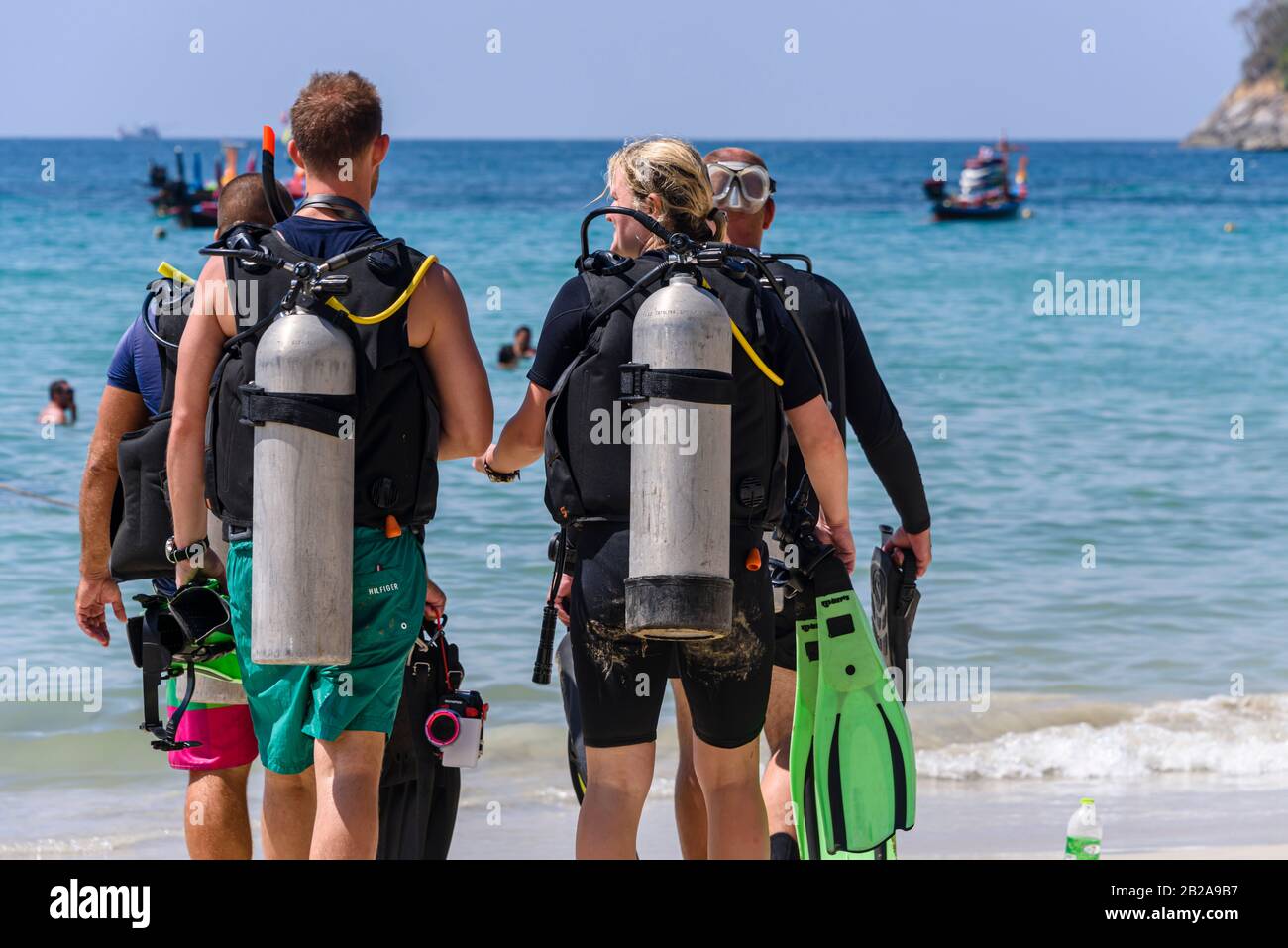 Quatre plongeurs avec des réservoirs de plongée marchent vers la mer à Kata Beach, Phuket, Thaïlande Banque D'Images