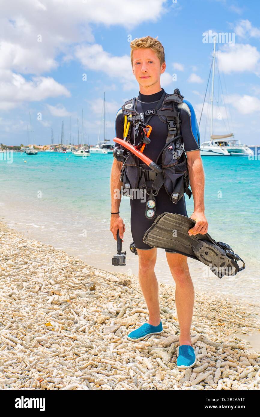 Plongeur masculin néerlandais posant sur la plage de Bonaire avec l'océan et les bateaux Banque D'Images