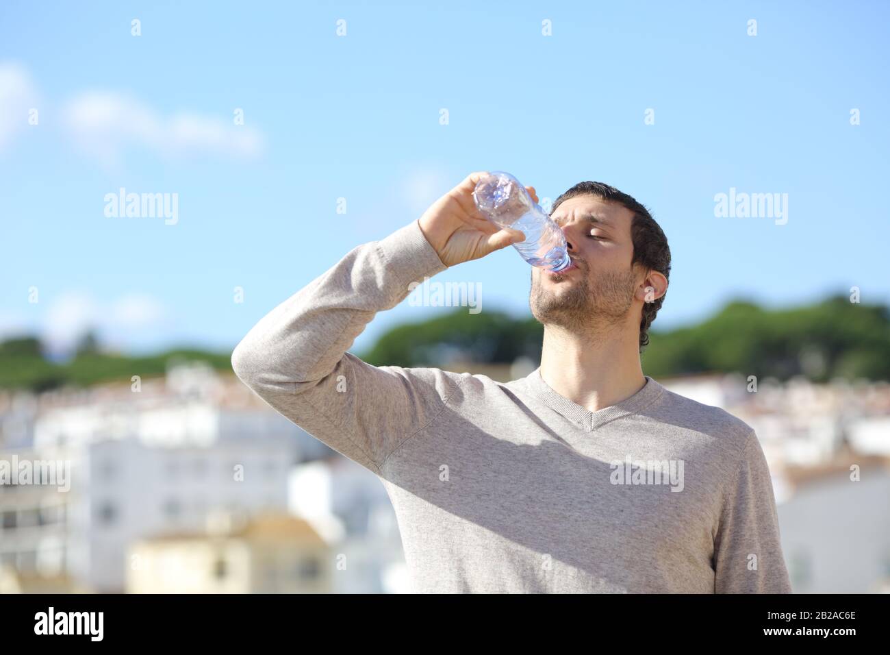 Homme buvant de l'eau embouteillée debout dans une ville une journée ensoleillée Banque D'Images
