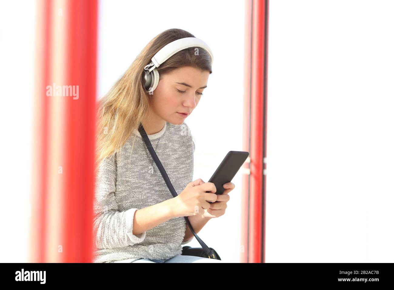 Une adolescente sérieuse écoute de la musique portant un casque sans fil et utilisant un smartphone dans un arrêt de bus Banque D'Images