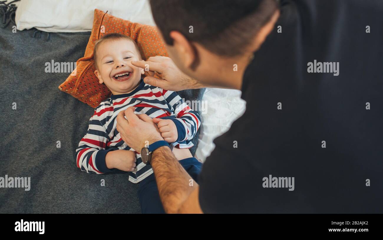 Le père caucasien ludique chatouille son petit fils qui courait sur le canapé et sourit joyeusement Banque D'Images