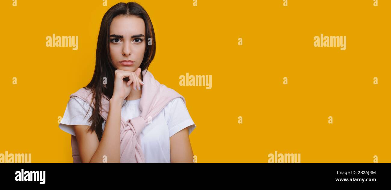La jeune fille caucasienne concentrée tenant son poing près du menton regarde malheureusement l'appareil photo tout en posant sur un mur jaune avec de l'espace libre Banque D'Images
