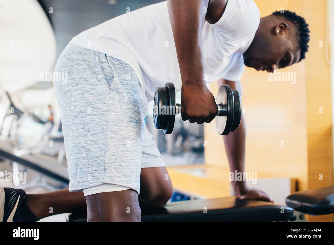 Vue latérale de l'homme africain américain dans les vêtements de sport se  penchant sur le banc et faire des exercices de rangée avec haltère pendant  l'entraînement dans la salle de gym Photo