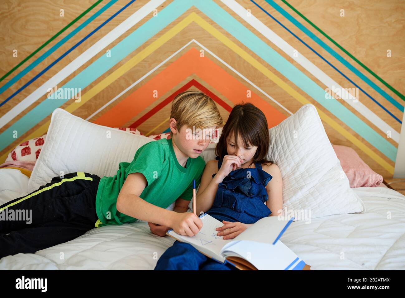 Garçon assis sur un lit pour aider sa sœur à faire ses devoirs Banque D'Images