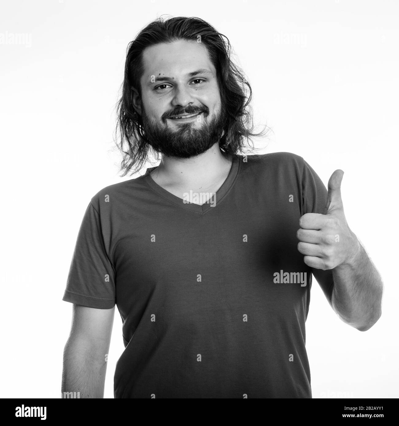 Studio shot of young happy barbu smiling while giving thumb up with long hair against white background Banque D'Images