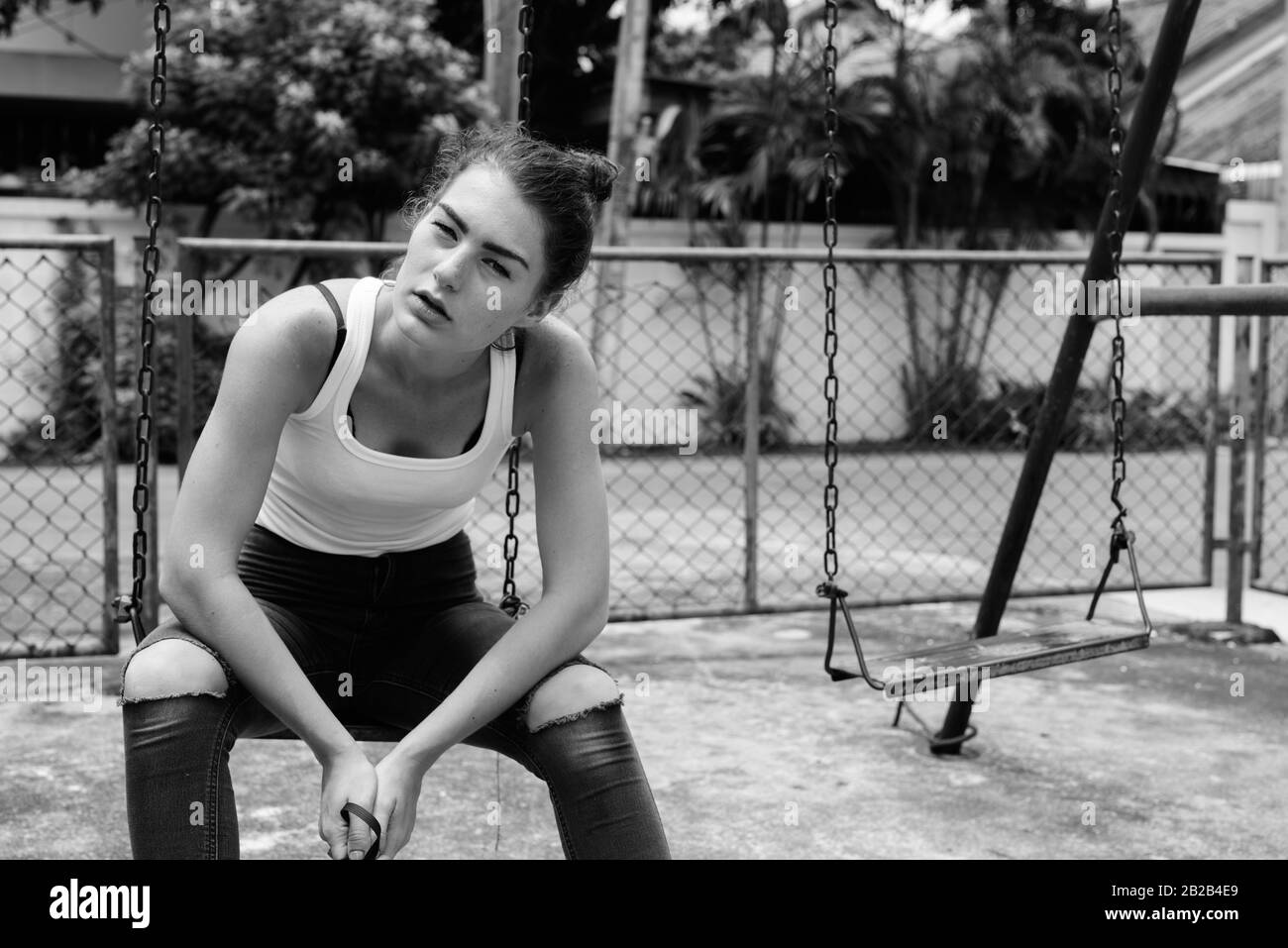 Young teenage girl sitting on the metal swing dans de vieux jeux pour enfants Banque D'Images