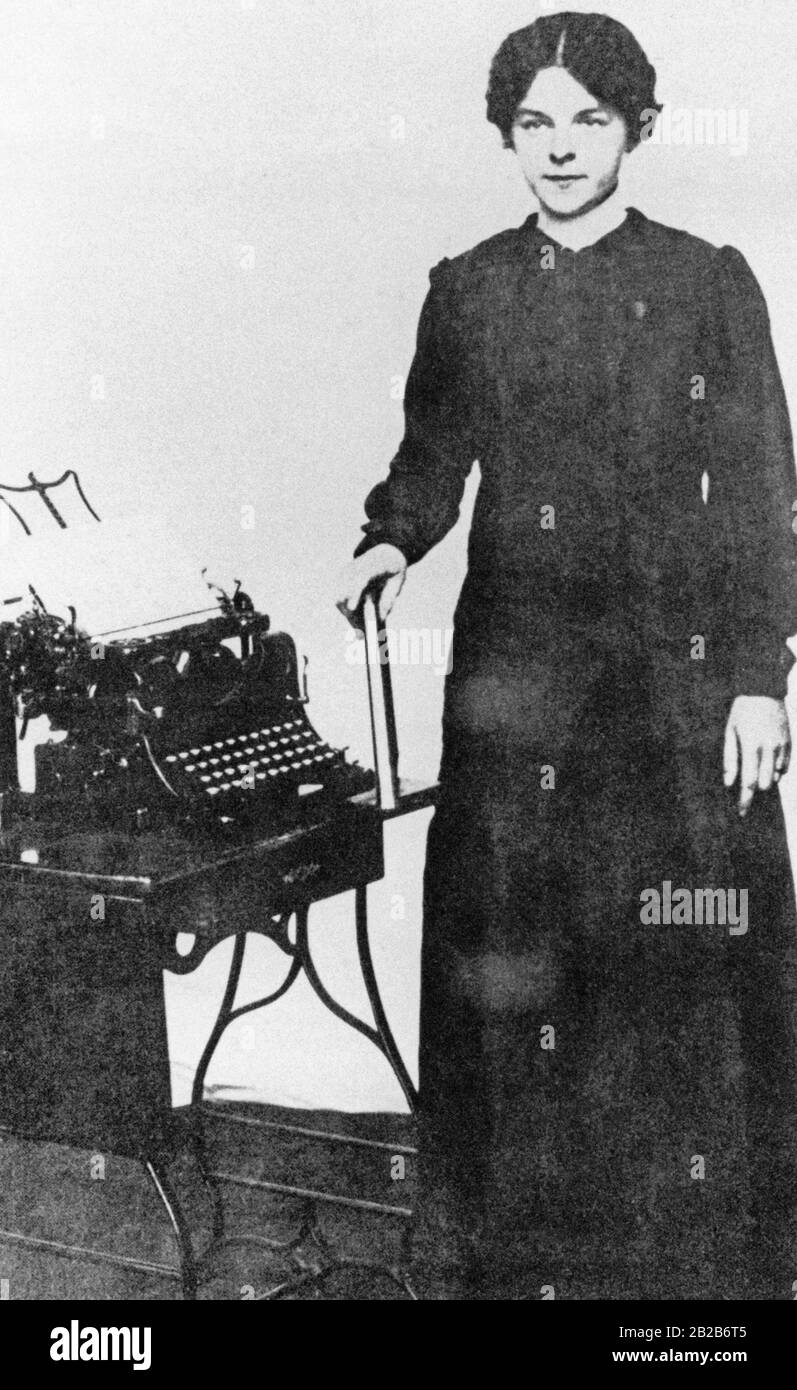 Une employée de bureau tenant un livre dans sa main, à côté d'elle est une machine à écrire debout sur une petite table. Photo non datée. Banque D'Images