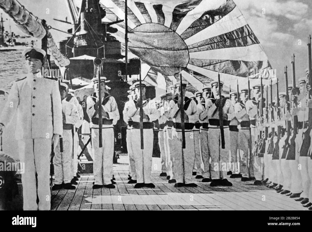 L'équipage d'un navire de la Marine impériale japonaise s'est aligné sur la terrasse. En arrière-plan, un grand drapeau de la Marine est en agitant. (Photo non datée, environ 1920) Banque D'Images