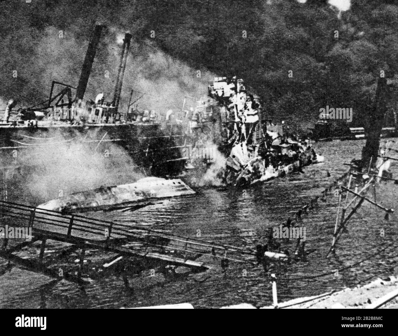 L'un des quais de Pearl Harbor après l'attaque japonaise du 07.12.1941. Les USS-Shaw détruits et les débris flottent dans l'eau. En arrière-plan il y a de la fumée noire. Banque D'Images
