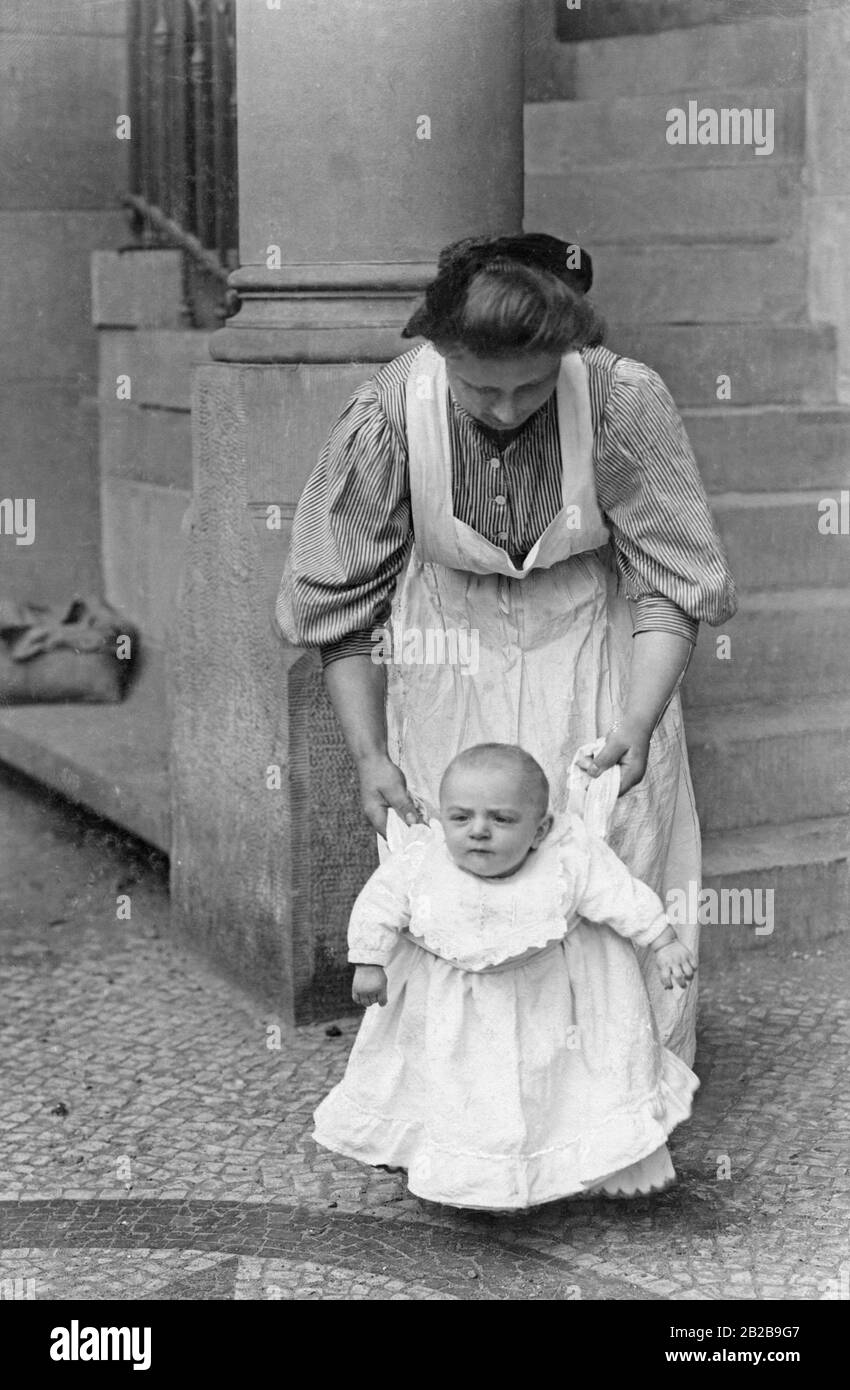 Un tout-petit apprend à marcher avec l'aide de sa nanny. Banque D'Images