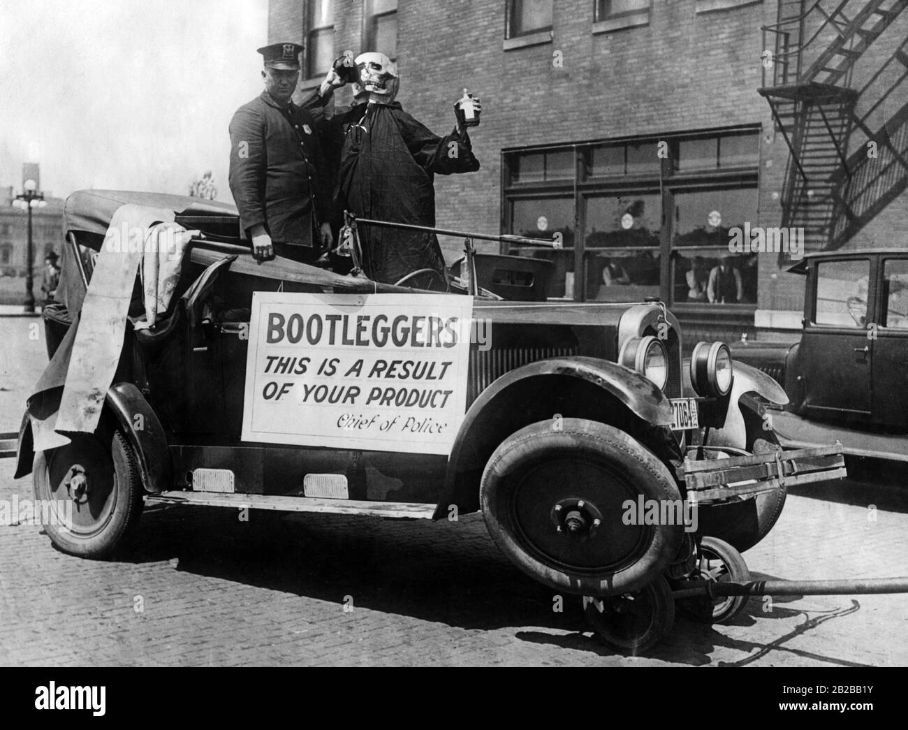 Campagne contre les bootleggers : un policier traverse la ville dans une voiture dans laquelle se tient un squelette buvant à partir d'une bouteille de liqueur. Un signe avec les mots: 'Bootleggers c'est un résultat de votre produit'. Banque D'Images