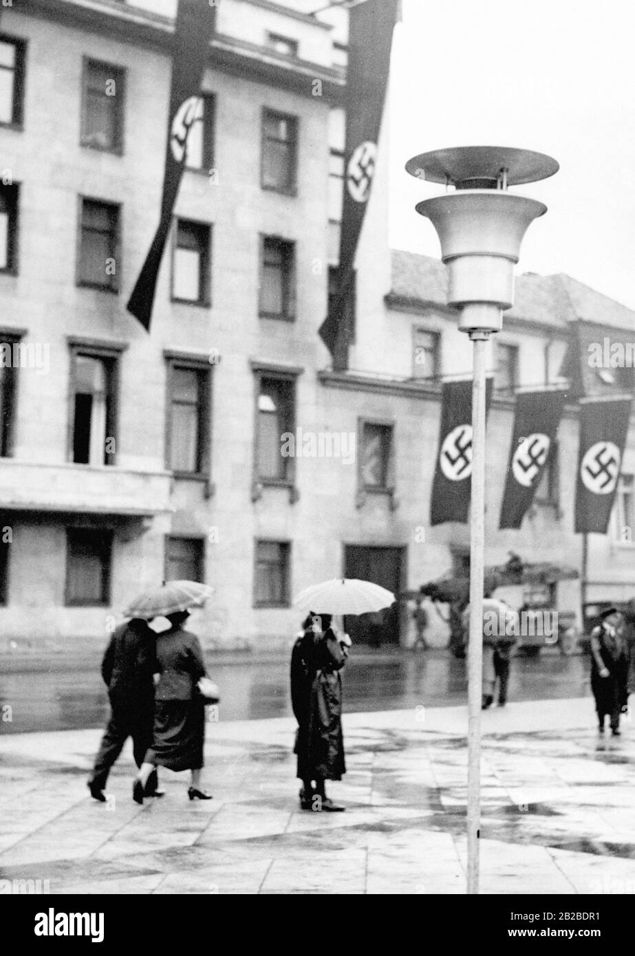 Les drapeaux à la vastika sont hoirés à l'extension de la Chancellerie du Nouveau Reich à Berlin. Passants à pied devant le bâtiment. Banque D'Images