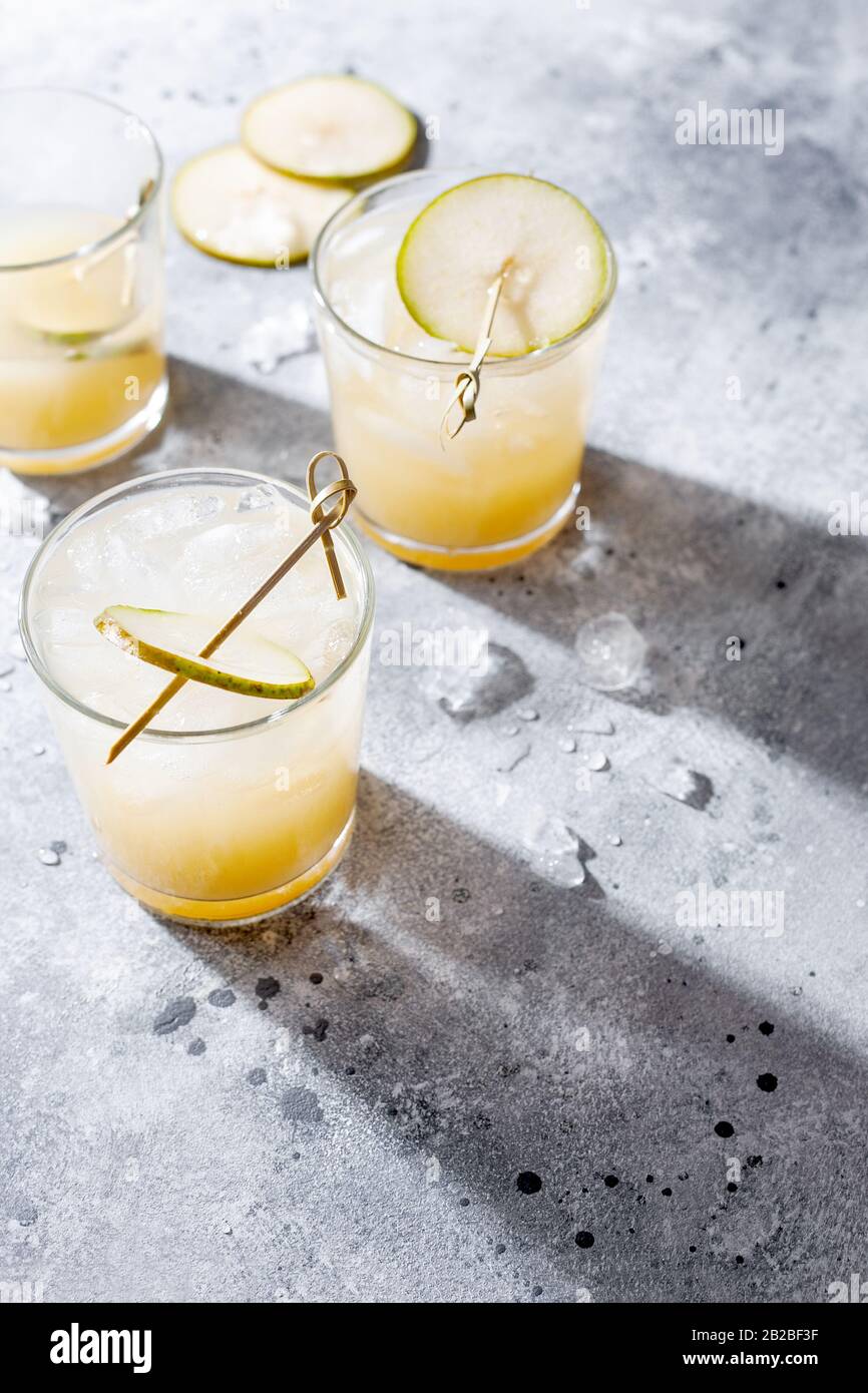 Cocktail de poire froide ou queue de bœuf avec purée de soda et de poire et tranches de fruits en verre court sur fond gris avec ombre. Boisson rafraîchissante en été Banque D'Images