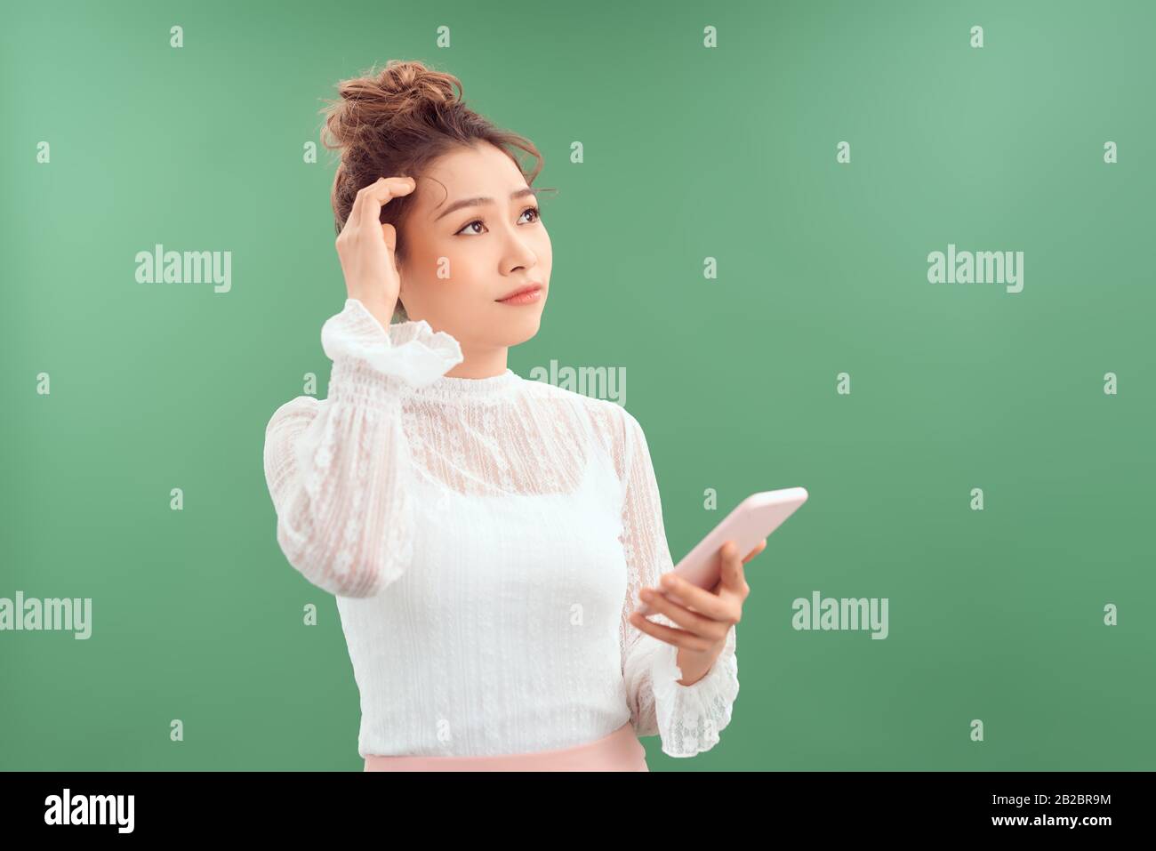 Portrait d'une jeune femme asiatique heureuse tenant un téléphone mobile tout en se tenant debout et en regardant isolé sur fond vert. Banque D'Images
