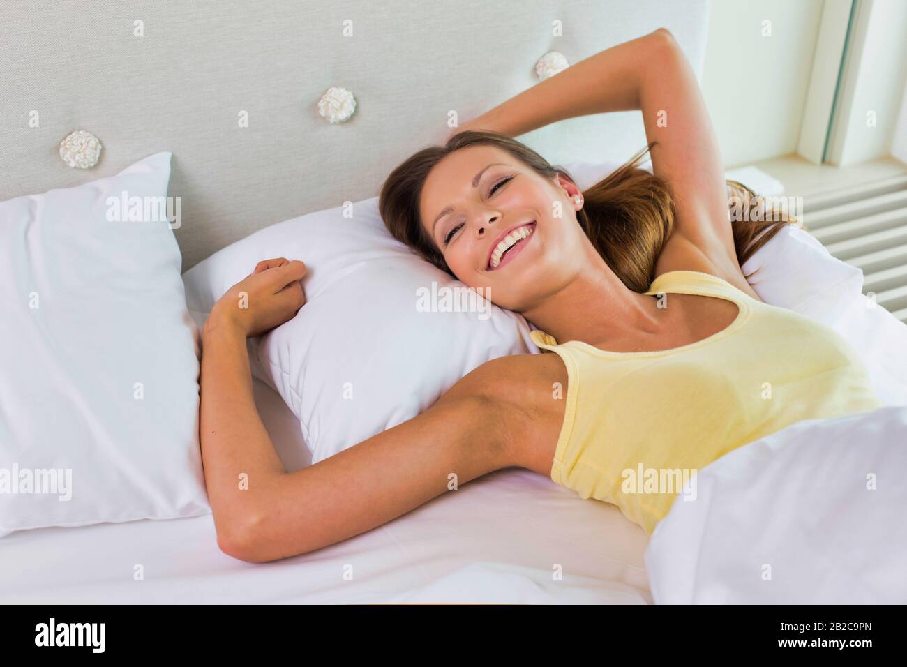 Jeune femme attrayante allongé tout en étirant ses bras dans le lit Banque D'Images