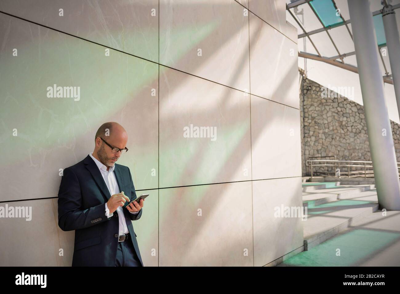 Portrait d'un homme d'affaires utilisant un smartphone tout en se penchant sur le mur Banque D'Images