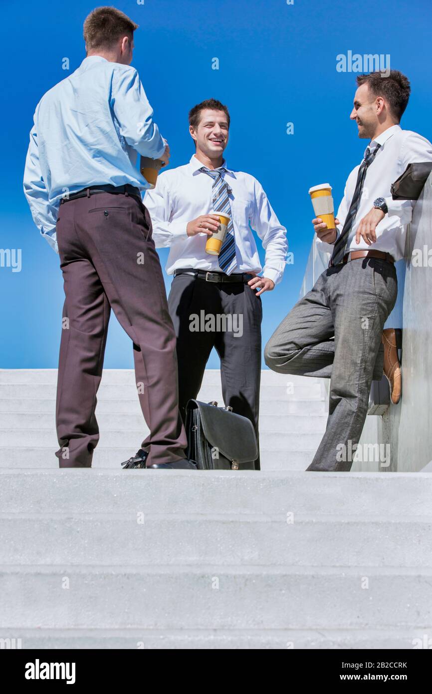 Groupe d'hommes d'affaires debout et parlant tout en buvant du café pendant la pause Banque D'Images Groupe d'hommes d'affaires debout et parlant tout en buvant du café pendant la pause Banque D'Images