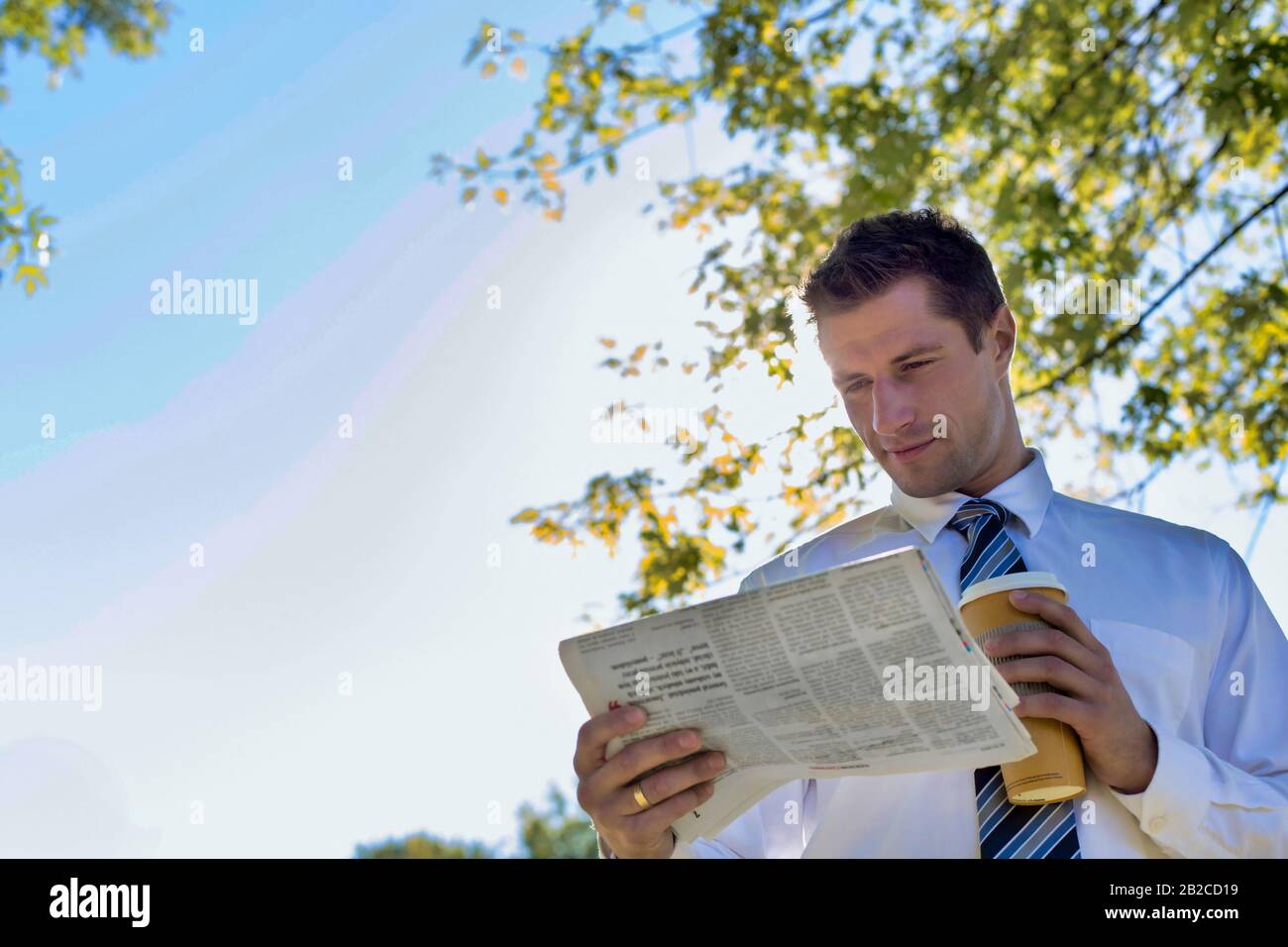 Portrait d'homme d'affaires mûr beau tenant une tasse de café tout en lisant le journal dans le parc pendant la pause Banque D'Images Portrait d'homme d'affaires mûr beau tenant une tasse de café tout en lisant le journal dans le parc pendant la pause Banque D'Images
