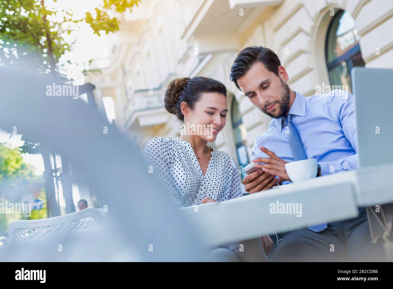 Homme d'affaires montrant un smartphone à une femme d'affaires tout en prenant un café pendant une pause au bureau Banque D'Images Homme d'affaires montrant un smartphone à une femme d'affaires tout en prenant un café pendant une pause au bureau Banque D'Images