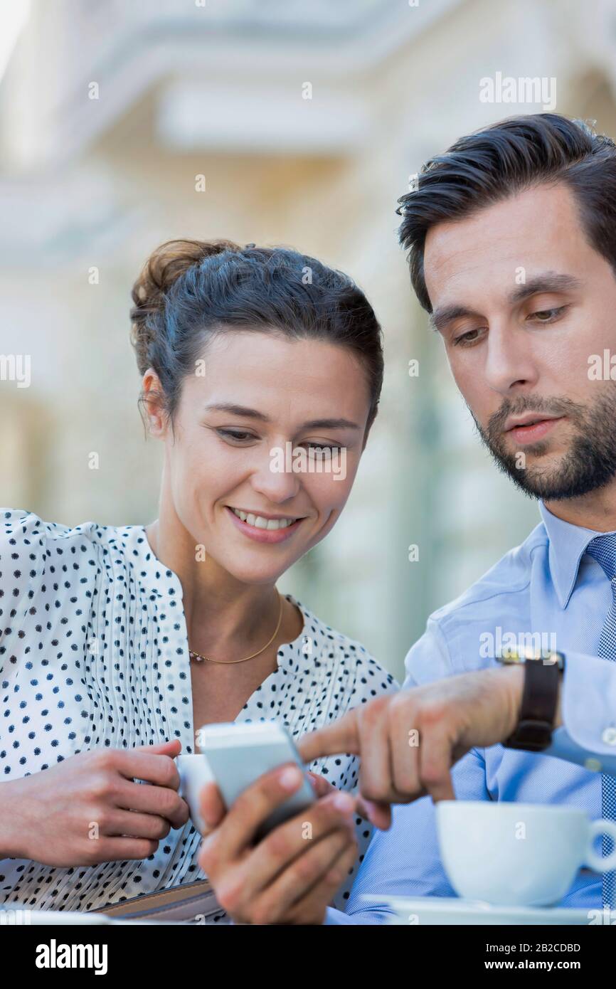 Homme d'affaires montrant un smartphone à une femme d'affaires tout en prenant un café pendant une pause au bureau Banque D'Images Homme d'affaires montrant un smartphone à une femme d'affaires tout en prenant un café pendant une pause au bureau Banque D'Images