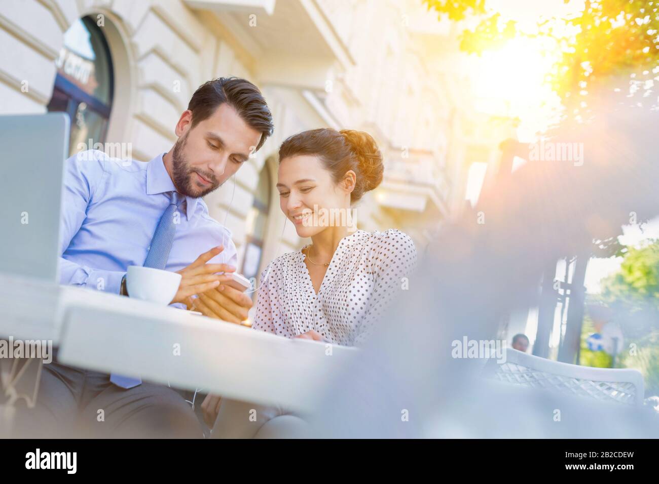 Homme d'affaires montrant un smartphone à une femme d'affaires tout en prenant un café pendant une pause au bureau Banque D'Images Homme d'affaires montrant un smartphone à une femme d'affaires tout en prenant un café pendant une pause au bureau Banque D'Images