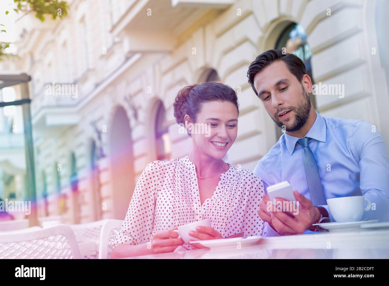 Homme d'affaires montrant un smartphone à une femme d'affaires tout en prenant un café pendant une pause au bureau Banque D'Images Homme d'affaires montrant un smartphone à une femme d'affaires tout en prenant un café pendant une pause au bureau Banque D'Images