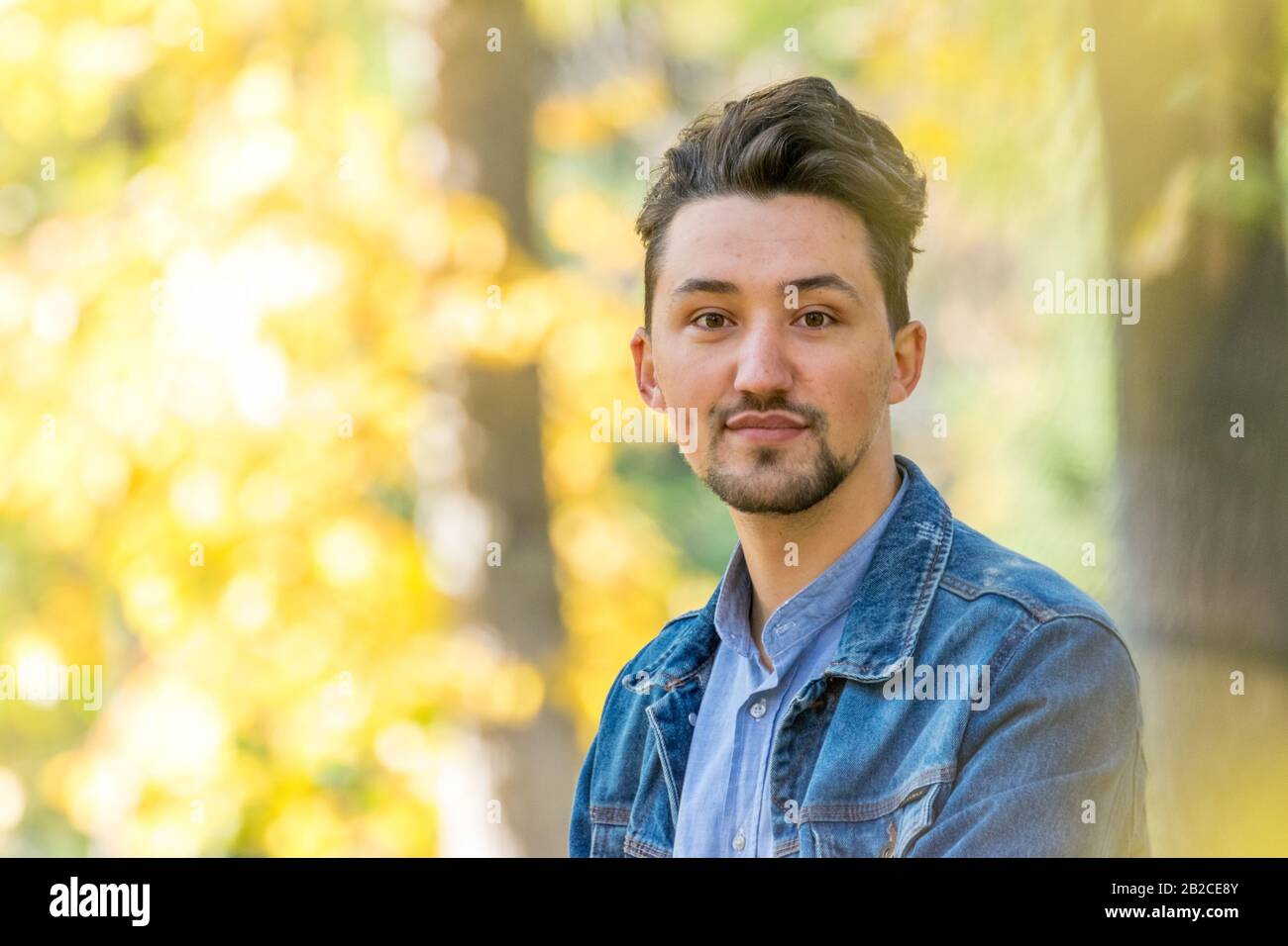 Beau jeune homme regardant l'appareil photo. Portrait d'un jeune homme confiant et réussi avec une veste denim et une chemise bleue à l'extérieur. Joyeux gars souriant Banque D'Images