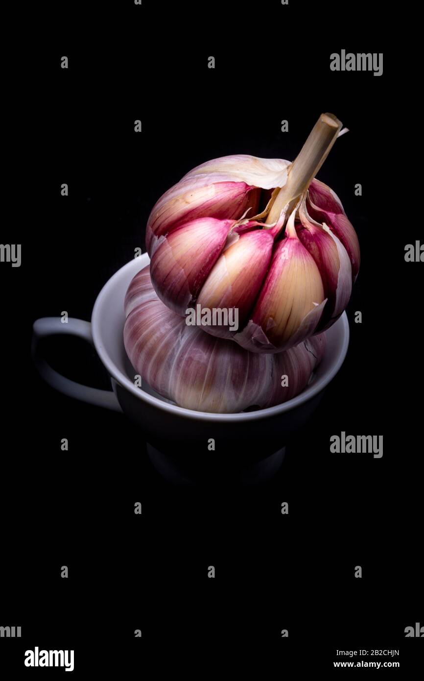 Ail rouge ou violet empilé dans une petite tasse blanche dans un cadre studio avec un fond clair et sombre spectaculaire vu du dessus Banque D'Images
