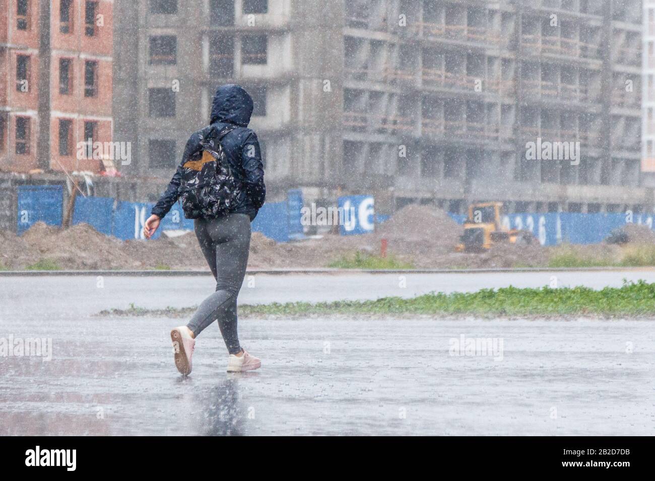 une femme avec un sac à dos et une capuche coule sous la pluie battante. Banque D'Images