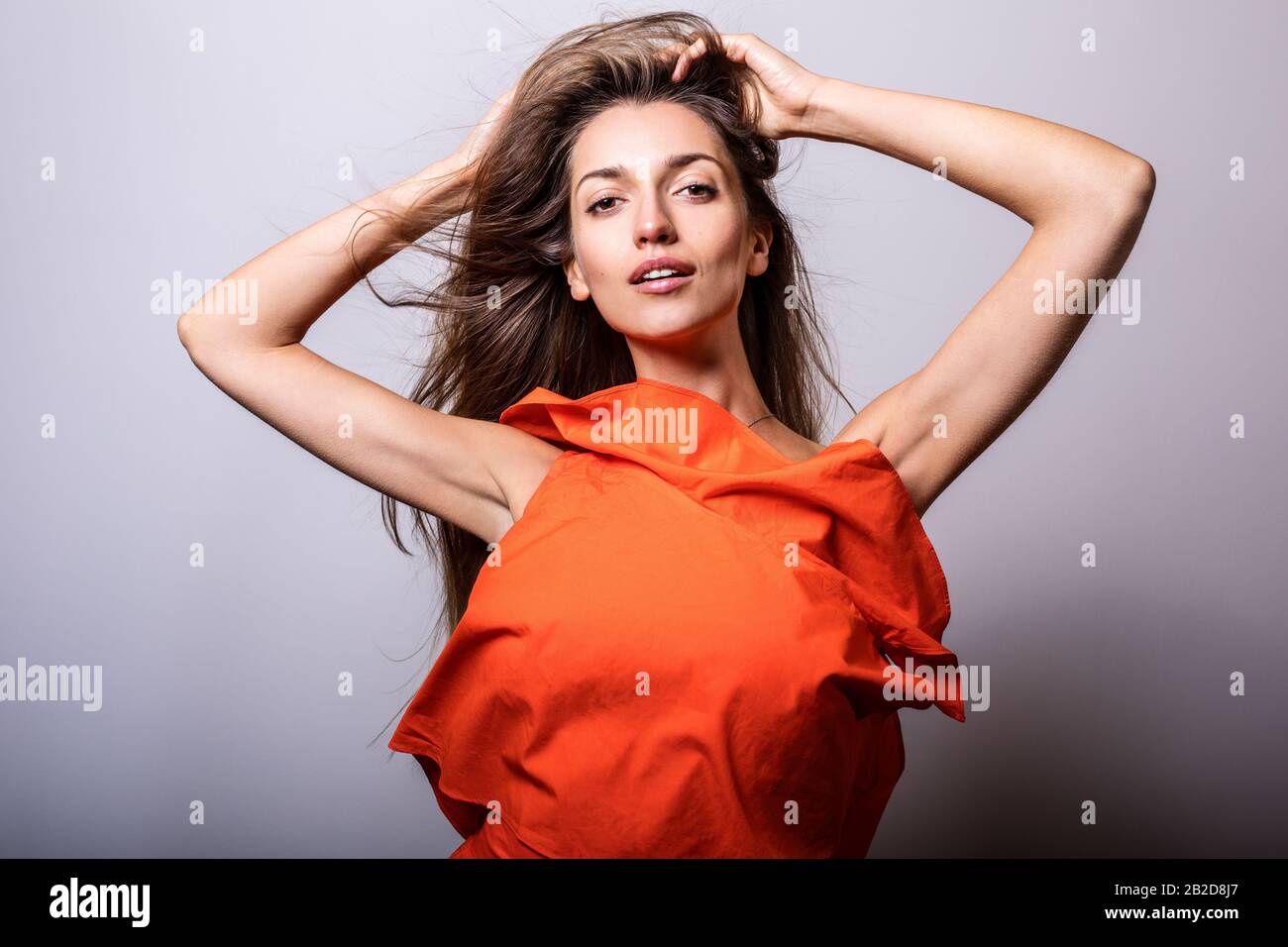 Jeune femme modèle en robe orange pose en studio. Banque D'Images