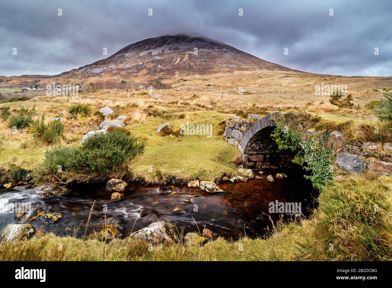 Vieux petit pont en pierre au-dessus de la rivière avec vue sur la montagne d'Errigal et les nuages de tempête, comté Donegal, Irlande Banque D'Images