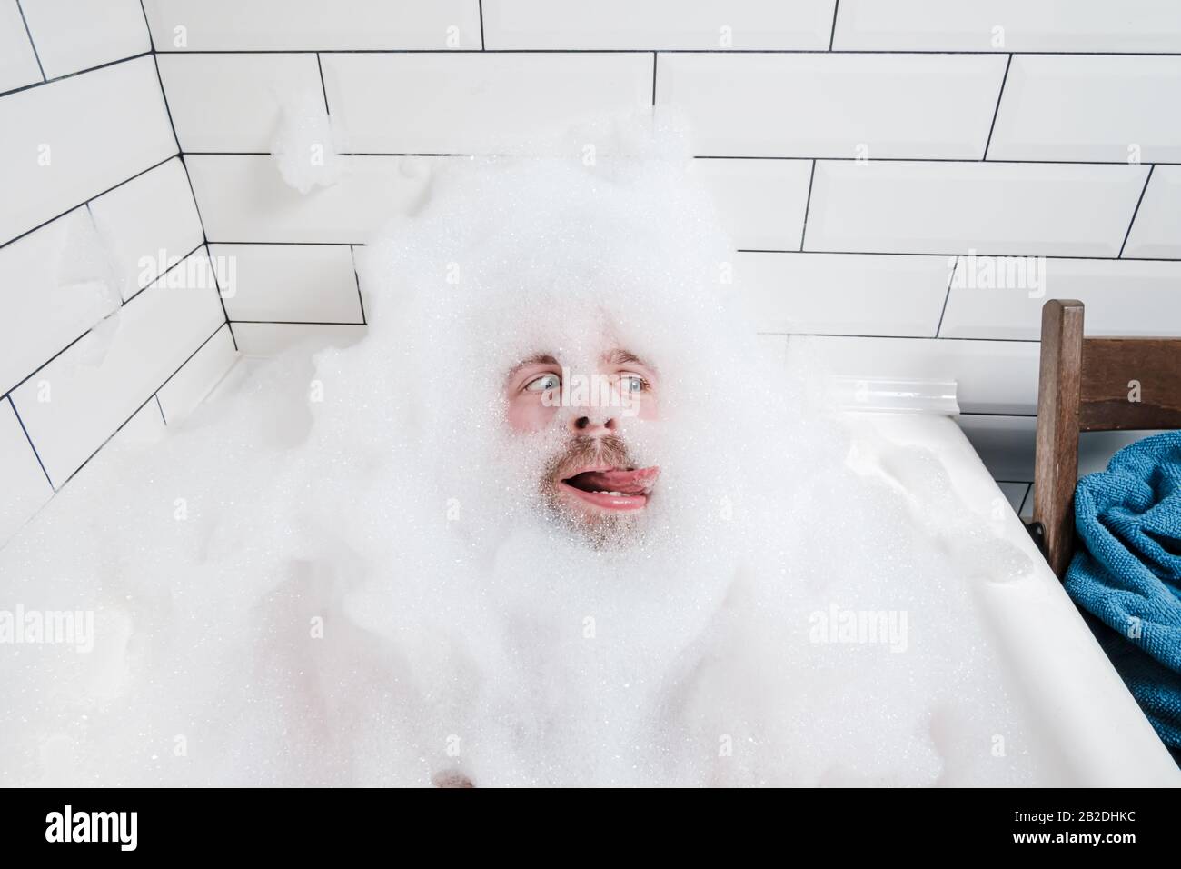 L'homme libre se trouve dans une baignoire avec de la mousse luxuriante et essaie avec sa langue. Banque D'Images